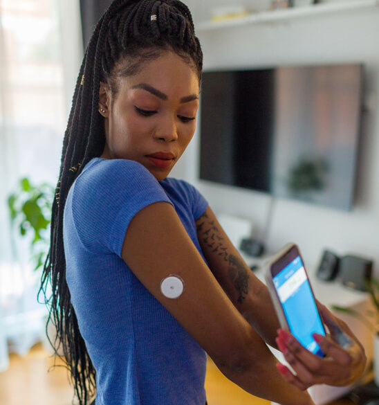 young woman scanning the continuous glucose monitor on her arm using her cell phone