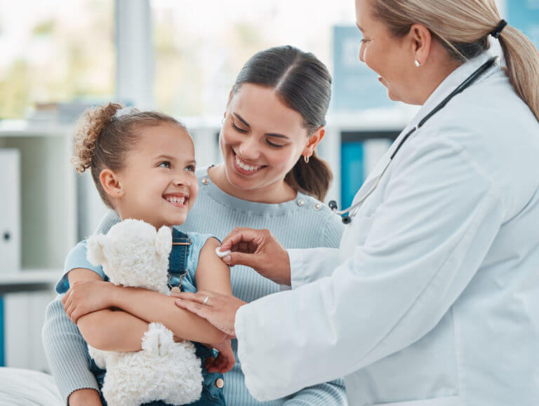 primary care doctor using a cotton ball on a little girl's arm while administering an injection in a clinic