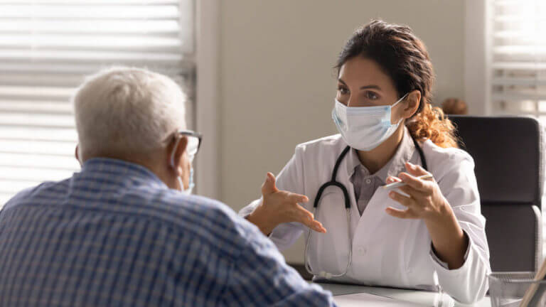 Close up female therapist wearing face mask consulting Senior at primary care