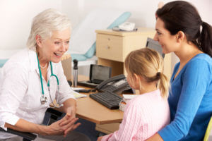 A senior female primary care doctor is speaking with a young child and her mother at the clinic.