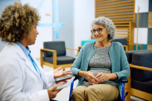 An elderly woman in a wheelchair talking to her primary care doctor at a medical clinic.