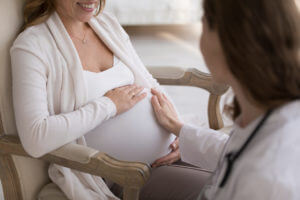 An obstetrician is gently touching the belly of a pregnant woman to offer support during her pregnancy.
