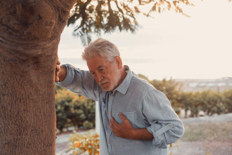 Close-up image of a sick old man at the park, touching his chest due to chest pain.