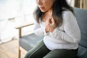 A mature woman is sitting on the sofa, experiencing heartburn.