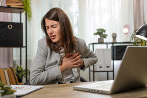 A businesswoman using a laptop suffers from tension and heart trouble, causing her to hold her chest in pain during a heart attack at the office.