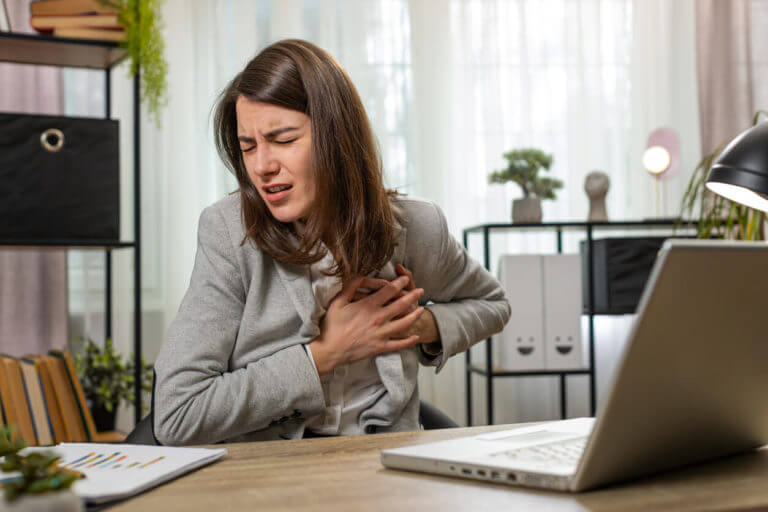 A businesswoman using a laptop suffers from tension and heart trouble, causing her to hold her chest in pain during a heart attack at the office.
