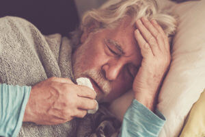 A senior man is feeling cold and is covering himself with a blanket due to pneumonia.