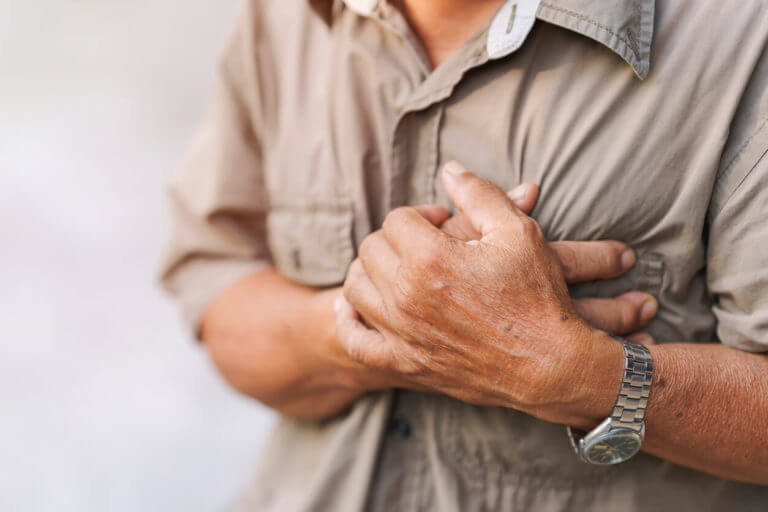 Close-up image of an elderly man's hand placed on his chest, showing signs of chest pain.