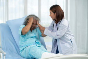 A female neurologist treats an elderly female patient who is holding her head in pain caused by migraines.