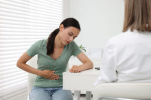 A GI Doctor consulting patient with stomach pain at table in clinic.
