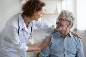 Smiling young primary care doctor supporting a senior patient with chronic condition.