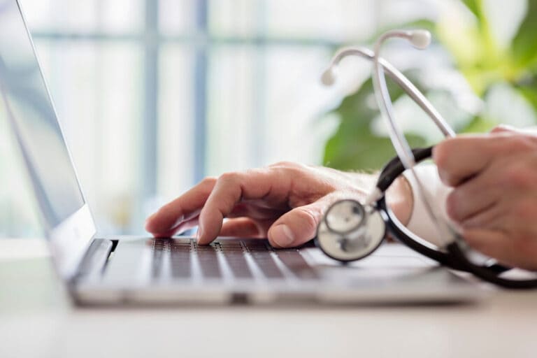 Primary care doctor entering patient notes on laptop.